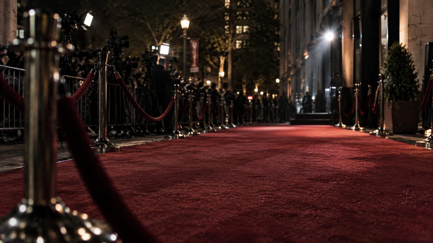 Empty red carpet at night with velvet ropes and soft camera flashes